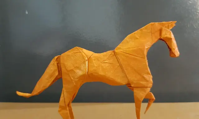 Ein orangefarbenes Origami-Pferd steht auf einem Tisch.