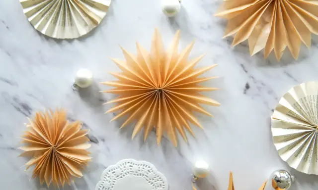 Fächersterne aus Papier, wie bei einer Teebeutel falten Anleitung, schmücken den Marmortisch neben Weihnachtskugeln.