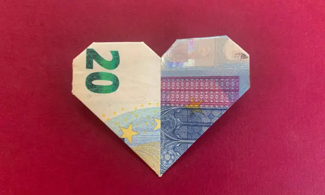 Ein gefaltetes Herz aus 20-Euro-Scheinen auf rotem Untergrund.