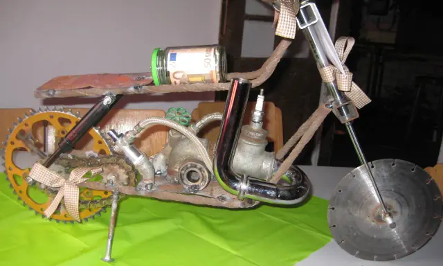 Kreatives Motorrad aus Altmetall, mit einem 50-Euro-Geldschein im Glas als Tank und einem kleinen Motorradhelm-Anhänger.