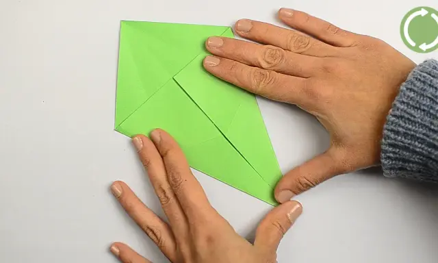 Hände falten ein grünes Papier, um einen einfachen Drachen zu basteln.
