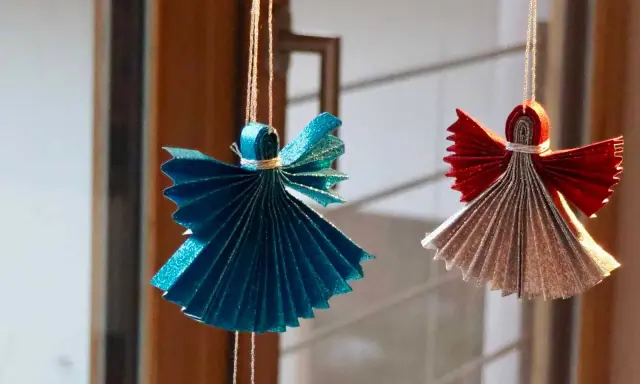 Zwei glitzernde Origami Weihnachts Engel, einer in Blau, der andere in Rot und Silber, hängen an Fäden.