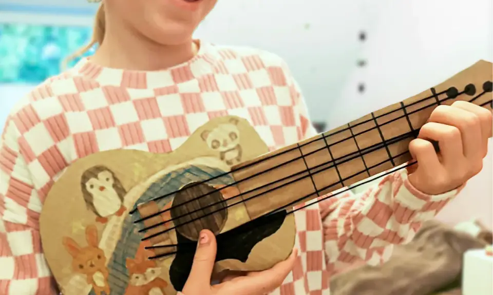 Kind bastelt Gitarre nach Vorlage. Die selbstgemachte Gitarre ist mit süßen Tieren wie Pinguin, Panda, Hase und Fuchs bemalt.