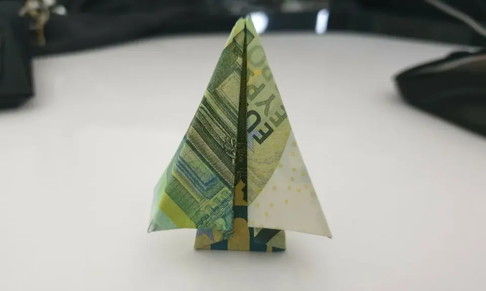 Ein kleiner, gefalteter Baum aus Geldscheinen steht auf einem Tisch. Ein kreativer geld falten baum.