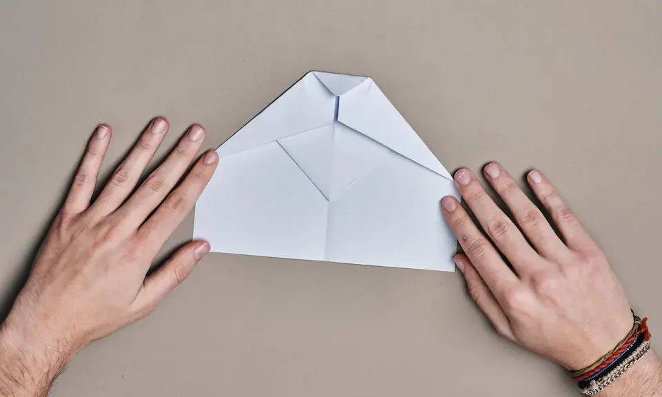 Hände falten einen weißen Papierflieger. Der runder Papierflieger nimmt langsam Form an.