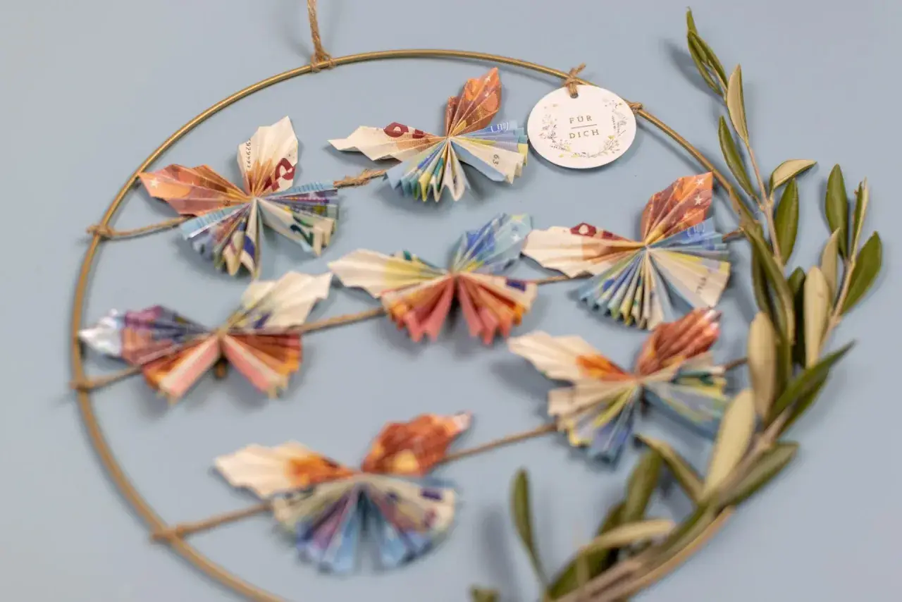 Kreative Deko: Viele bunte Schmetterlinge, gefaltet aus Geld, hängen an einem Ring. Ein schönes Geschenk, um Freude zu schenken.