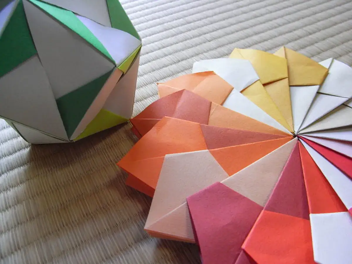 Origami Kugel Anleitung: Bunte Papierf&auml;cher und eine gr&uuml;ne Origami-Kugel auf einer Tatami-Matte.