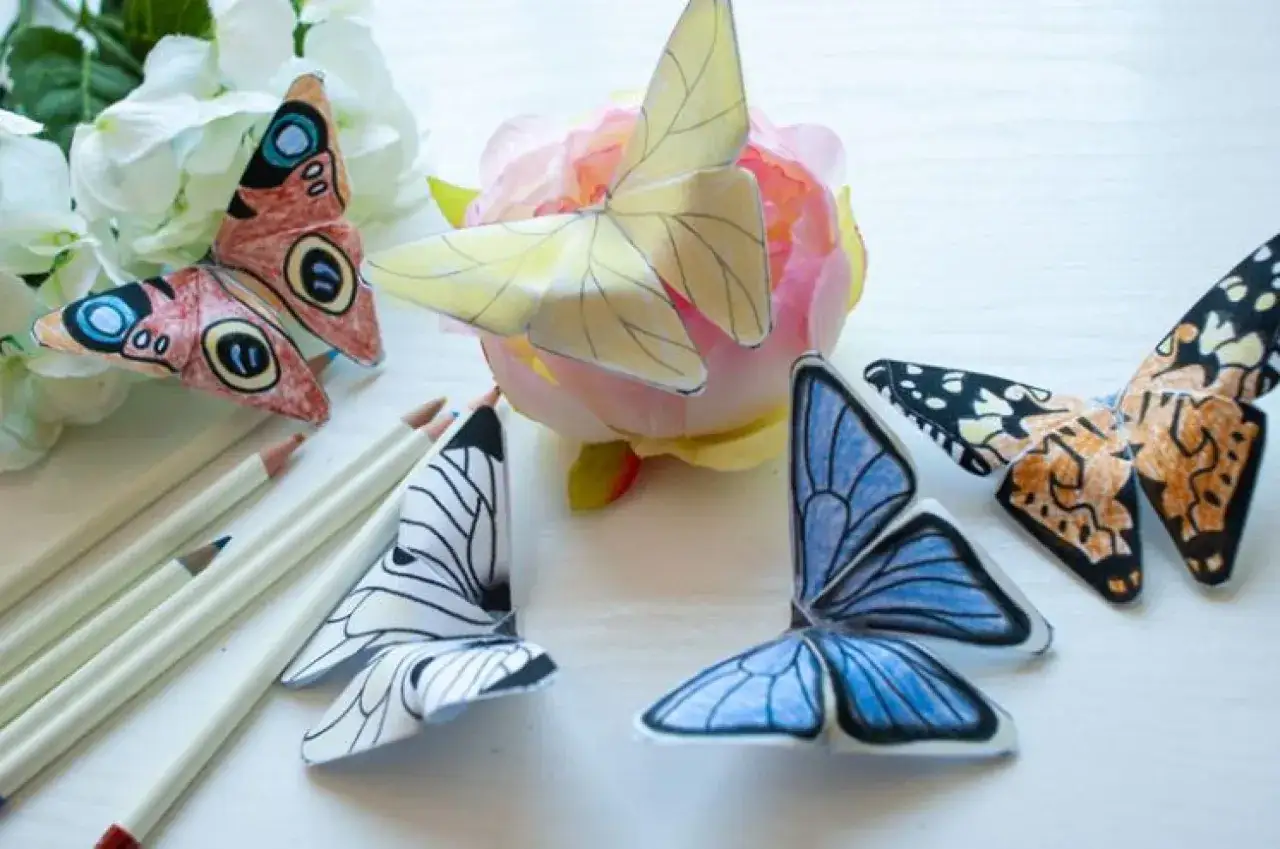 Bunte Papier-Schmetterlinge, die zum Schmetterling basteln einladen. Buntstifte liegen bereit.