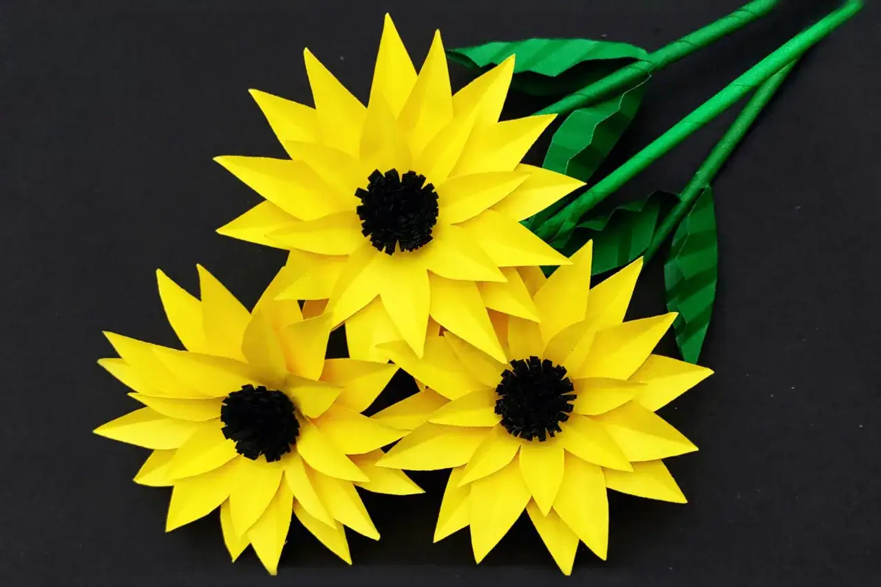 Drei gelbe Papier-Sonnenblumen mit schwarzen Zentren und grünen Stielen, ideal als sonnenblume basteln vorlage.