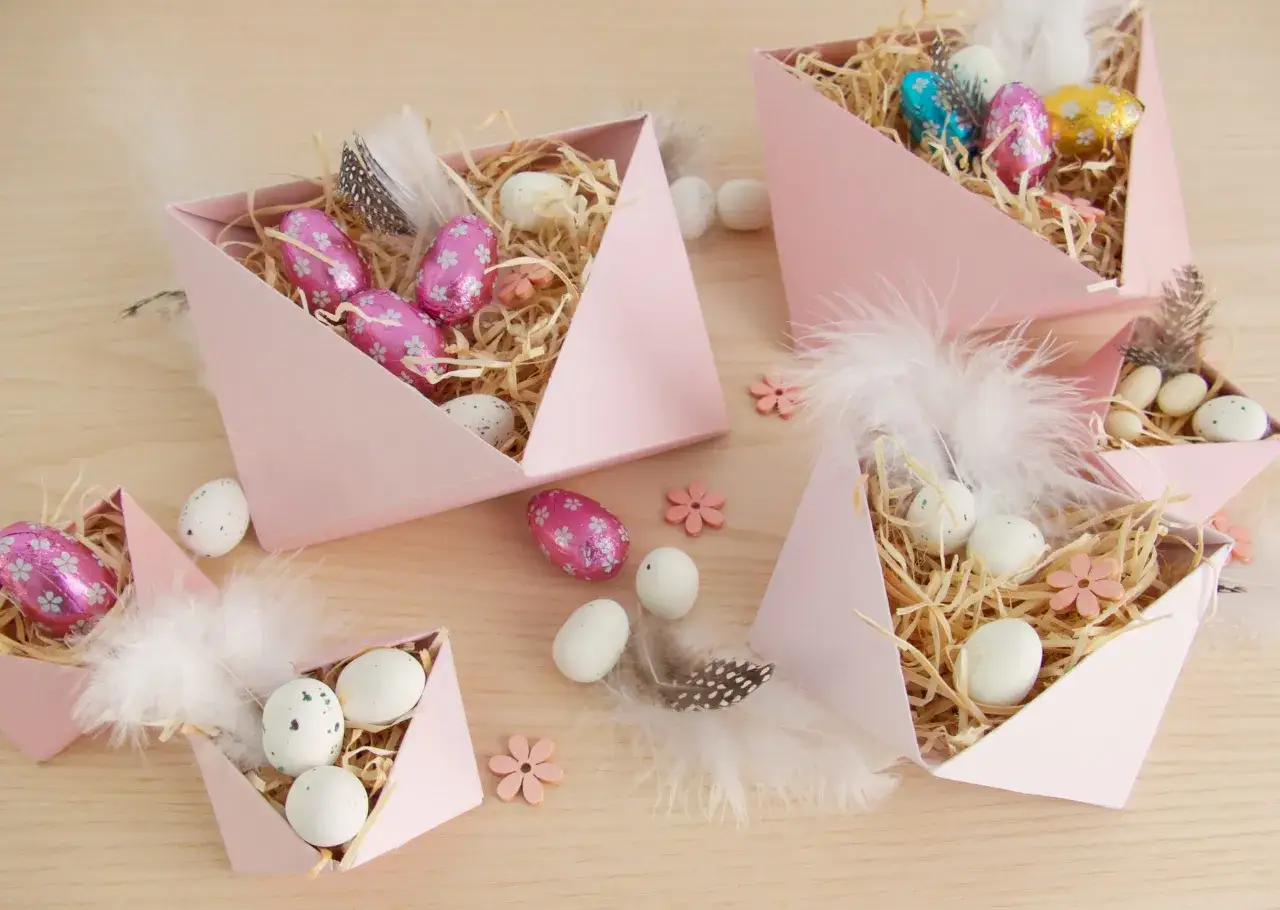 DIY Osternest-Ideen: Rosa Schachteln gef&uuml;llt mit Stroh, bunten Schokoladen- und echten Eiern, Federn und kleinen Holzblumen.