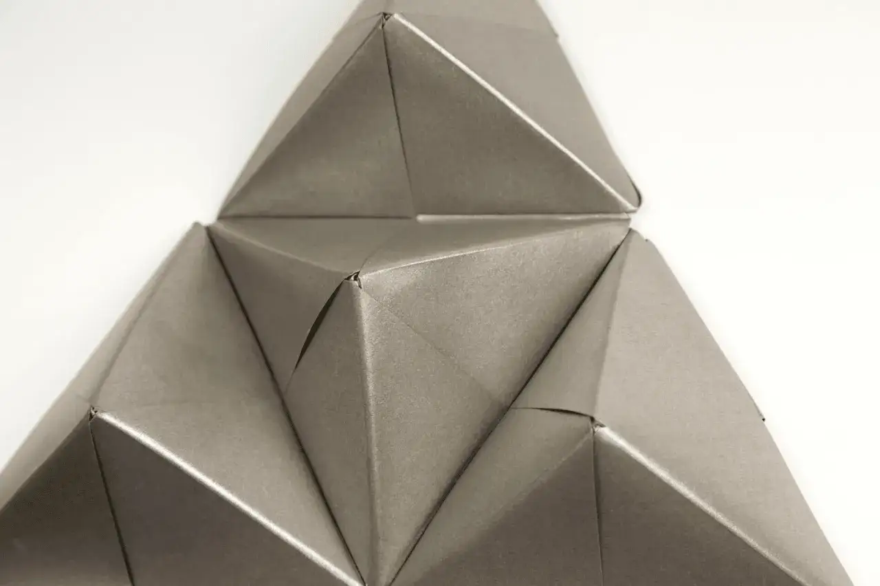 Detailaufnahme von komplexem, modularem Origami in Grau. Die geometrischen Formen und Falten erzeugen ein faszinierendes Muster.