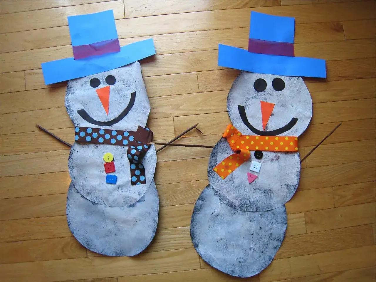 Zwei selbstgebastelte Schneem&auml;nner mit blauen H&uuml;ten und bunten Schals, bereit f&uuml;r den Winter. Perfekt zum Schneemann basteln!