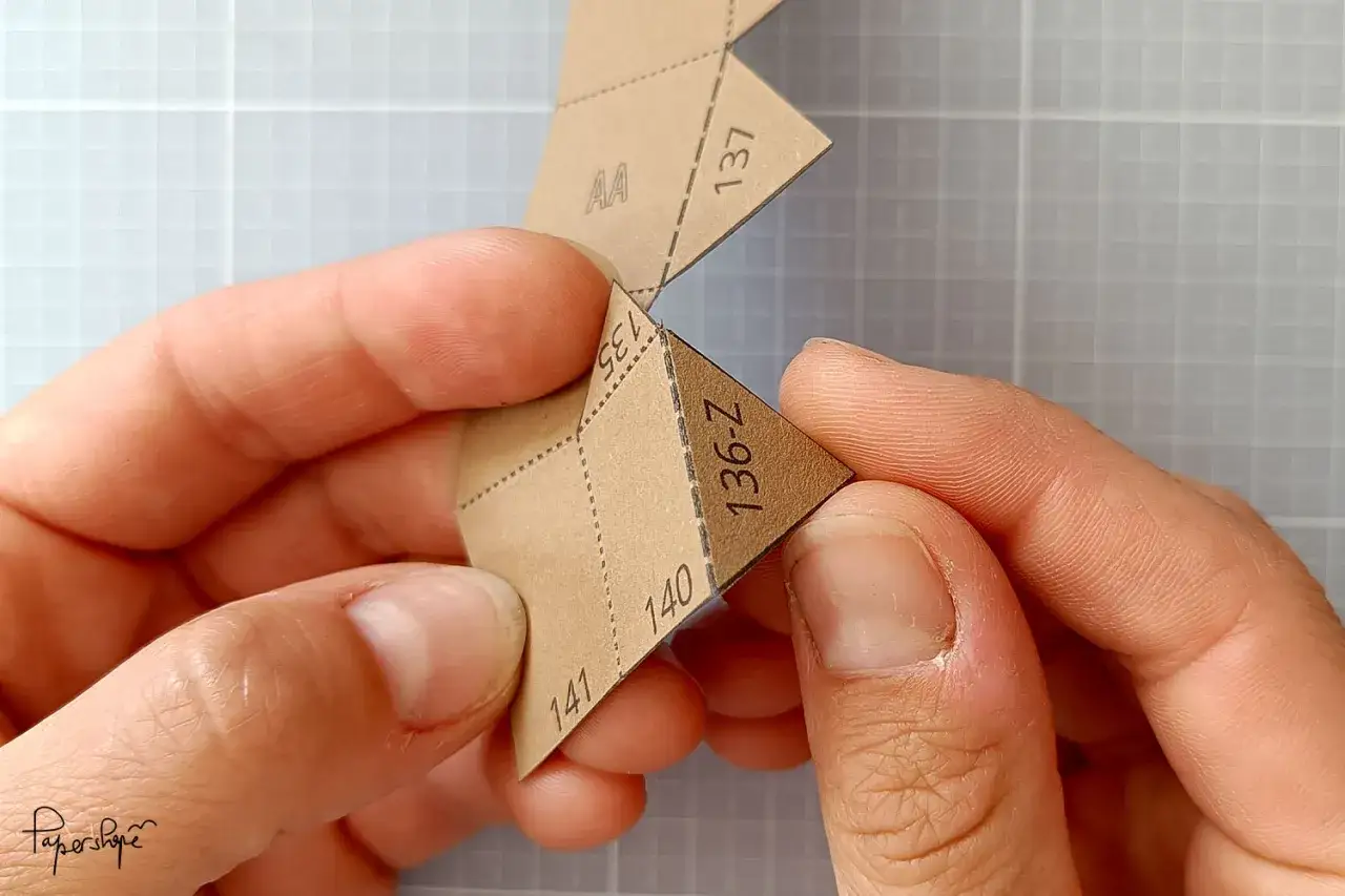 H&auml;nde falten ein Papier mit Zahlen und Buchstaben. Die Anleitung zum berge aus papier falten wird pr&auml;zise befolgt.