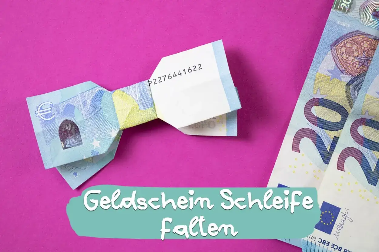 Geld falten Schleife: Ein gefalteter Geldschein in Form einer Schleife liegt auf einem pinken Untergrund. Daneben liegen weitere Geldscheine.