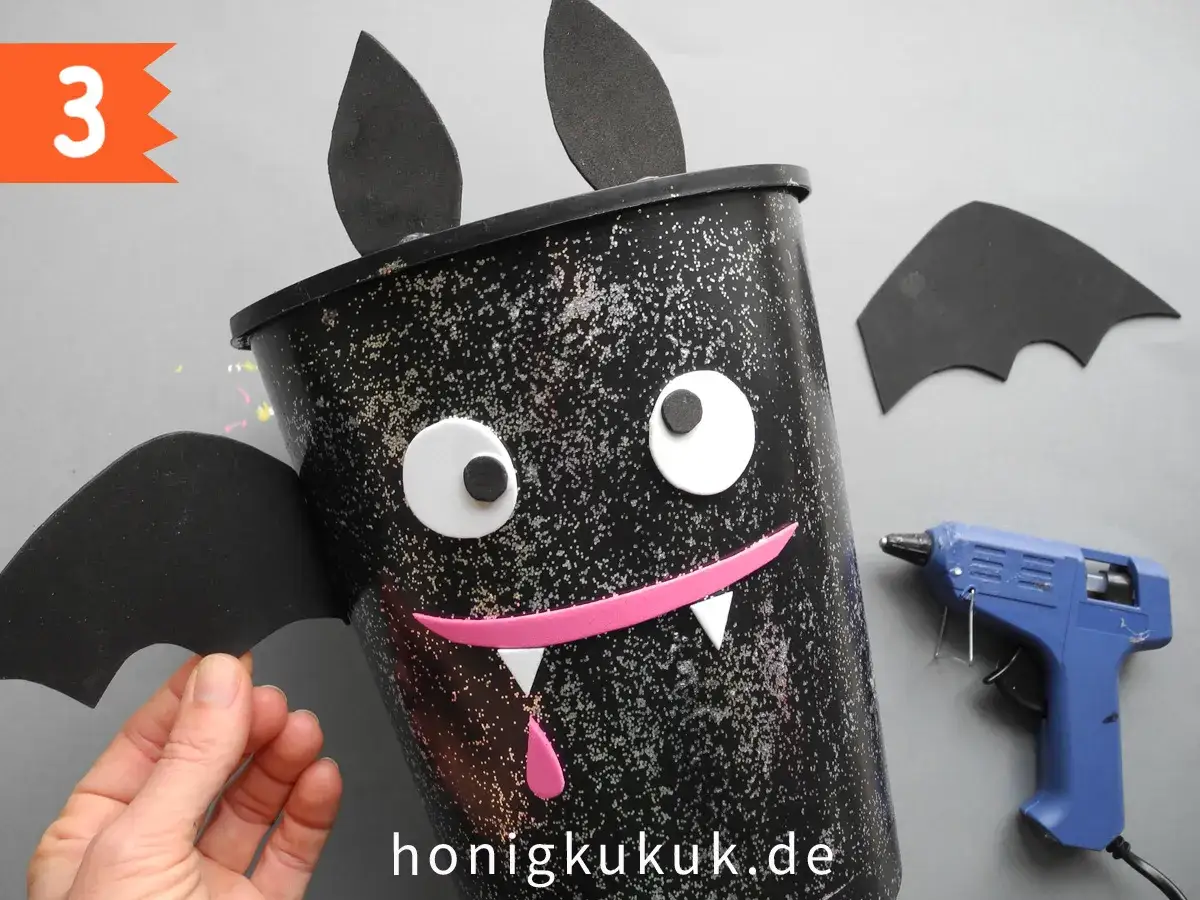 Schritt 3: Ein Fledermaus-Halloween-Eimer basteln. Mit Klebepistole und Bastelmaterialien entsteht ein gruseliger Hingucker.