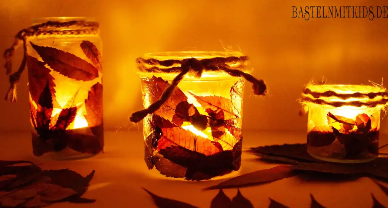 Drei leuchtende Windlichter, gebastelt mit Papier und Herbstbl&auml;ttern, strahlen warmes Licht aus. Ein sch&ouml;nes Bastelprojekt f&uuml;r Kinder.