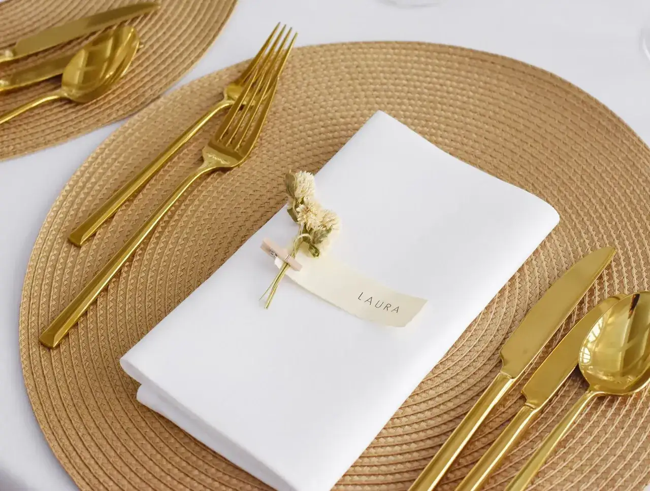 Elegante Tischdekoration mit goldener Besteckgarnitur und sorgfältig gefalteten Servietten. Ein Namensschild mit 