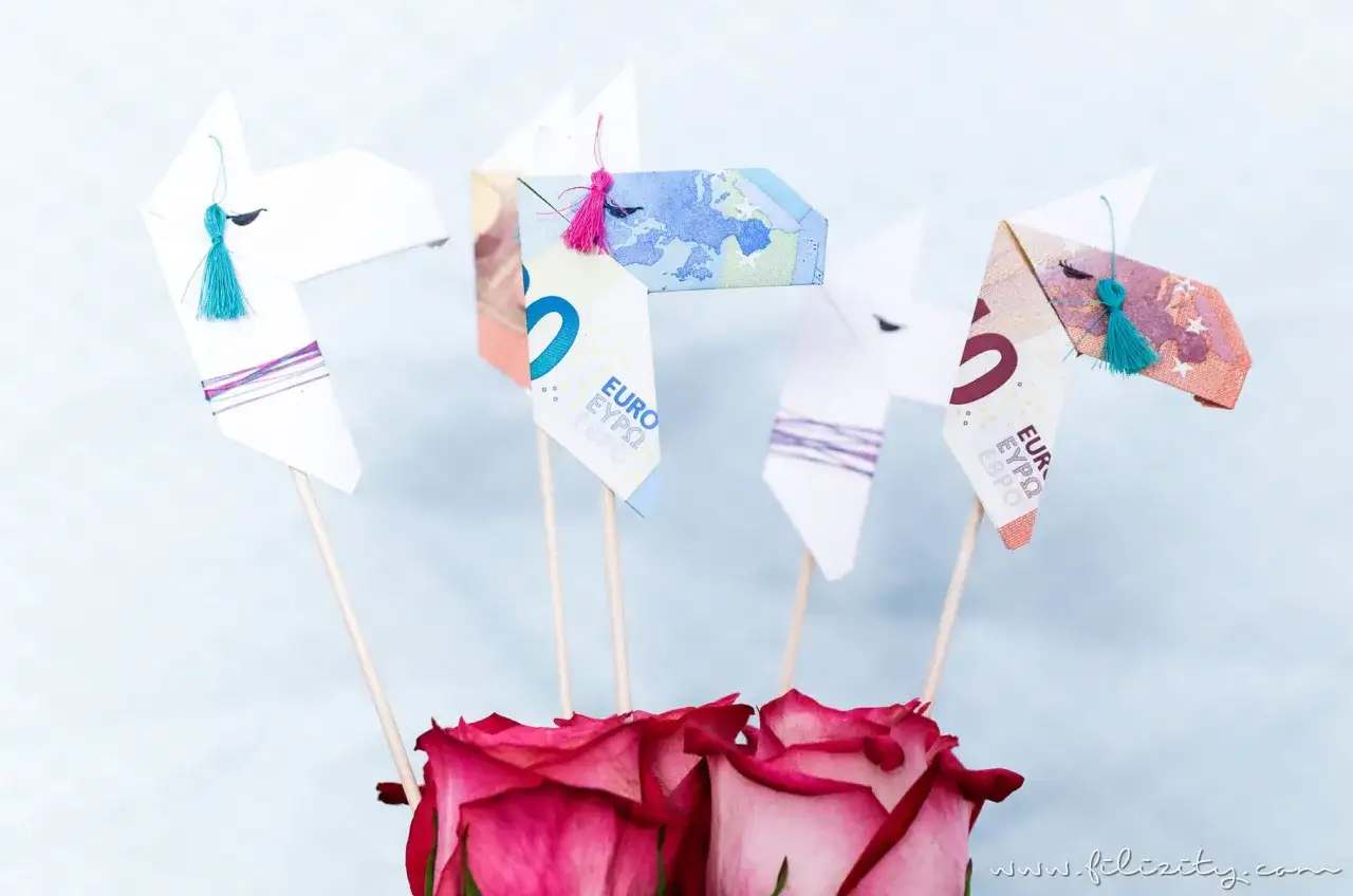 Origami-Pferde aus Geld gefaltet, mit bunten Quasten und Rosen. Ein kreatives Geldgeschenk.