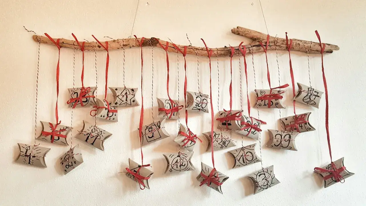 Kreativer Adventskalender aus Klorollen, nummeriert und mit roten Bändern verziert, hängt an einem Ast.