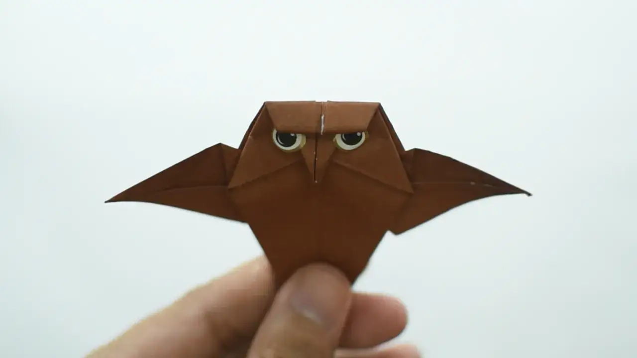 Eine braune origami eule mit großen Augen wird von einer Hand gehalten.