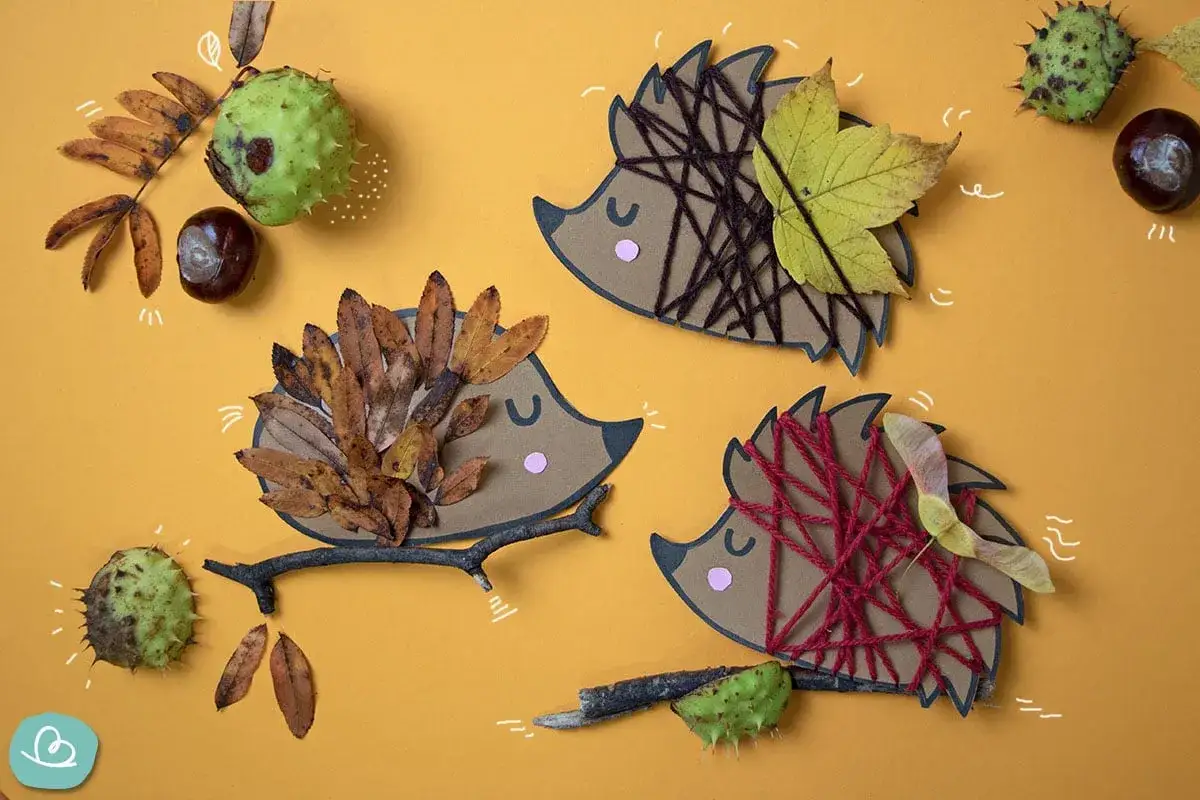 Drei Igel-Bastelvorlagen aus Papier, Wolle und Herbstlaub. Ein Igel tr&auml;gt ein Blatt, ein anderer Herbstlaub, der dritte ist mit roter Wolle verziert.