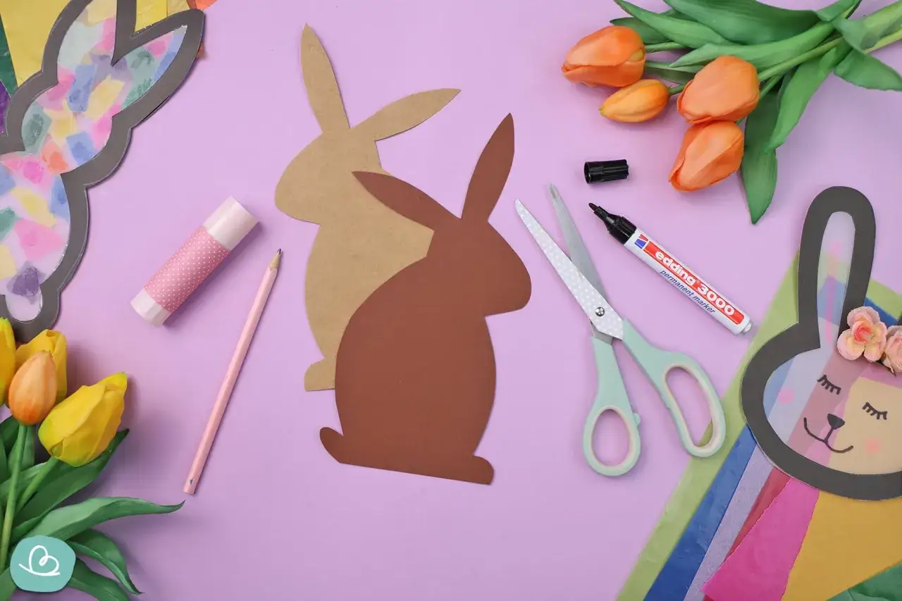 Bastelmaterialien für einen Osterhasen aus Tonpapier: Schere, Stift, Kleber, Papierhasen-Vorlage und bunte Tulpen.