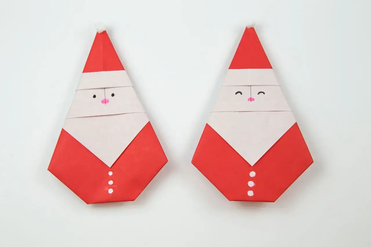 Zwei niedliche Origami-Nikol&auml;use mit roten M&auml;nteln und wei&szlig;en B&auml;rten, bereit f&uuml;r den Winter.