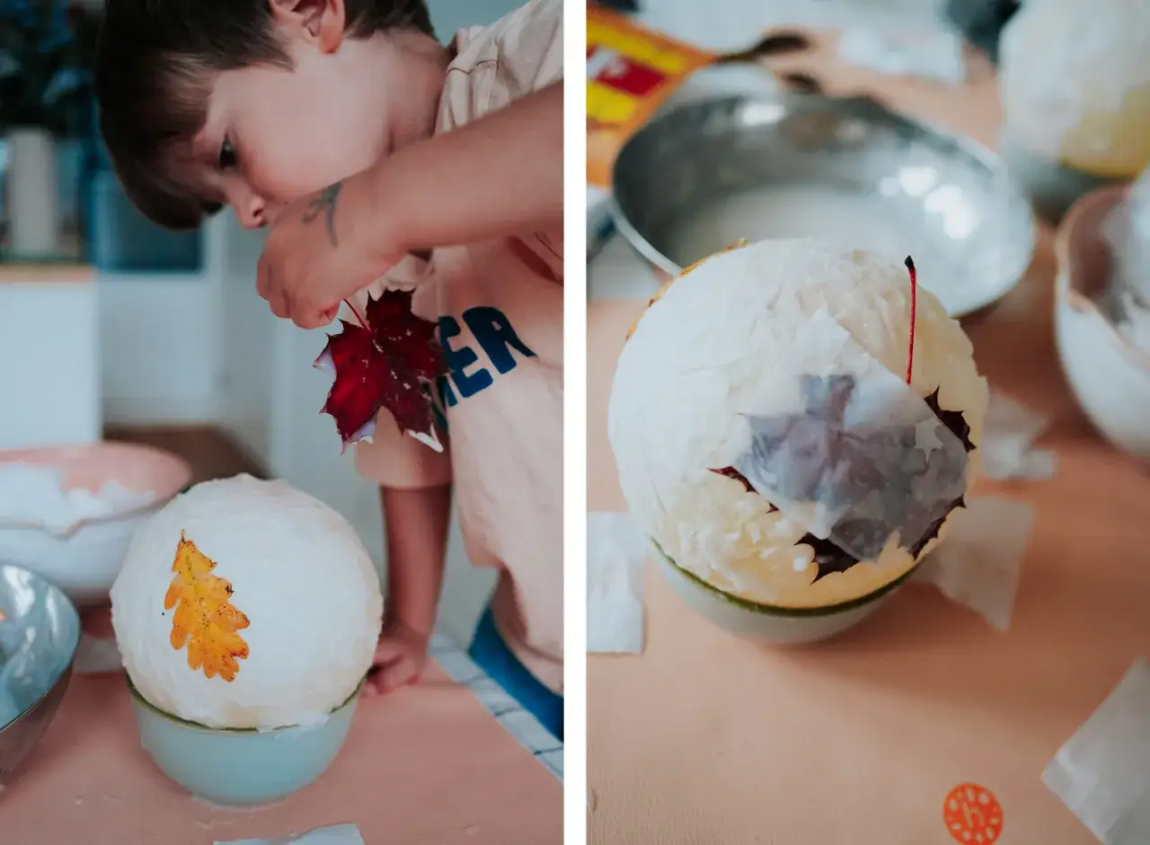 Kind bastelt eine Laterne mit Luftballon und Kleister. Bunte Bl&auml;tter werden aufgeklebt.