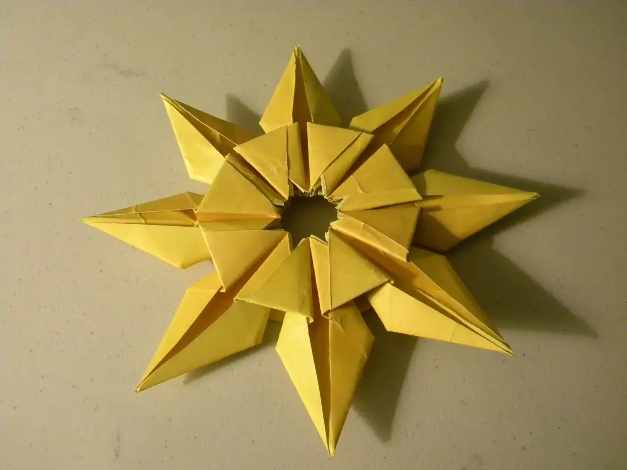 Ein gelbes Origami-Sternchen, das wie eine kleine origami sonne aussieht, liegt auf einer hellen Oberfl&auml;che.