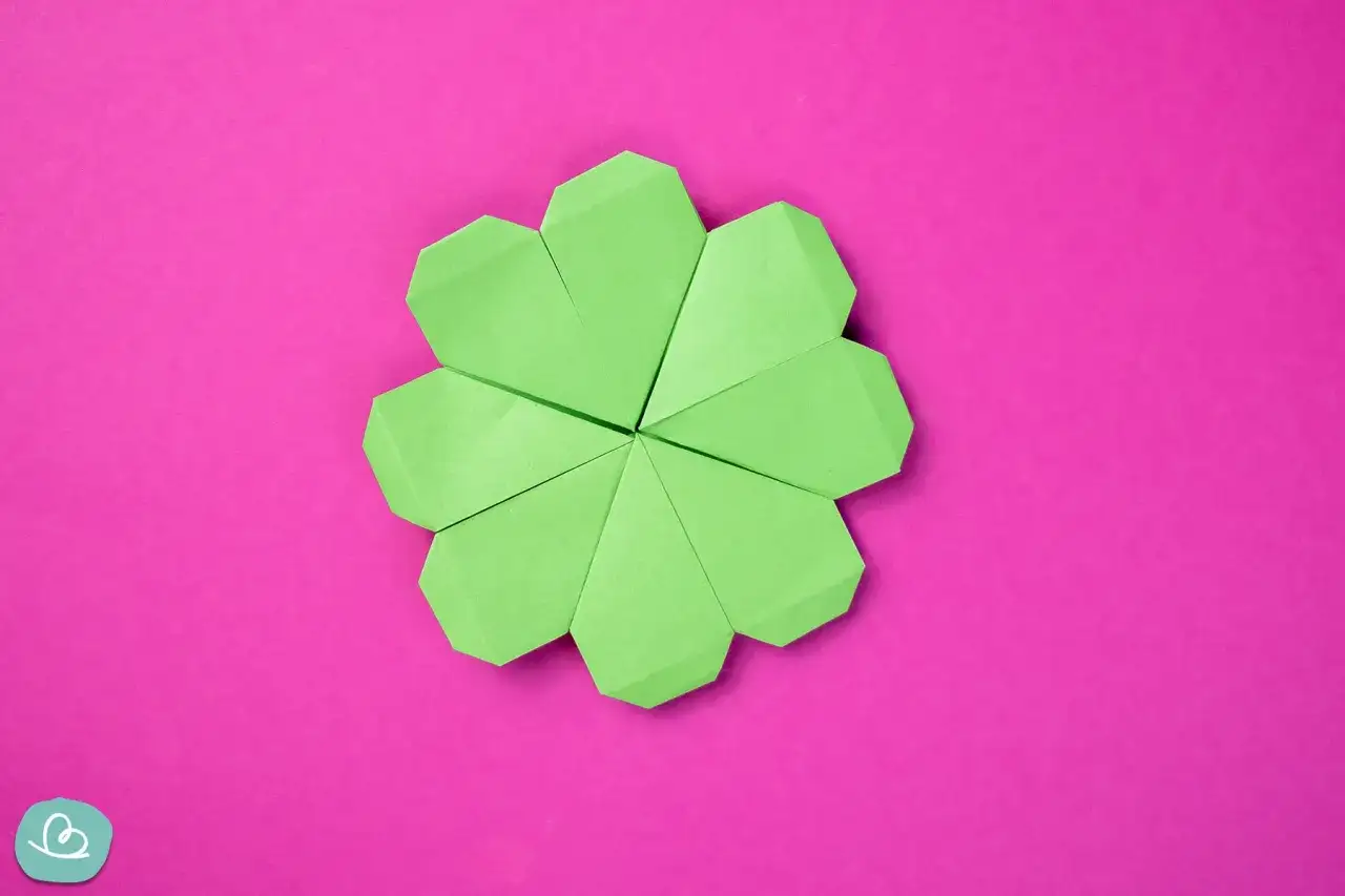 Ein grüner Origami-Glücksbringer, der wie ein Kleeblatt aussieht, liegt auf einem pinken Hintergrund.