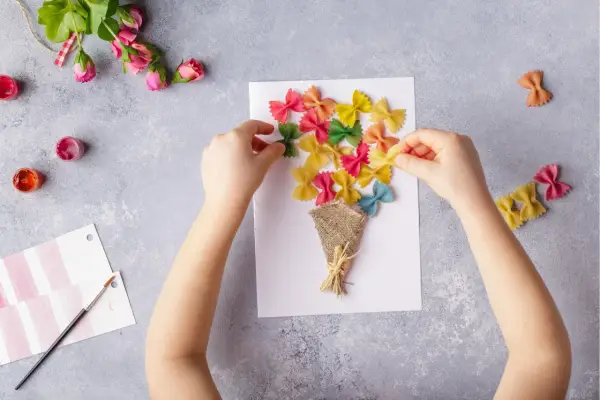 Kinder basteln eine bunte Geburtstagskarte mit farbiger Pasta als Blumenstrauß.