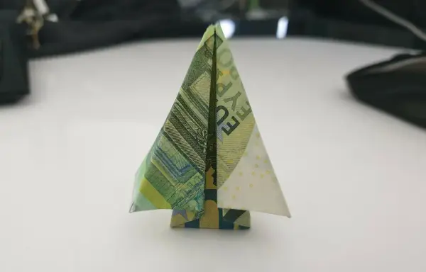 Ein kleiner, gefalteter Baum aus Geldscheinen steht auf einem Tisch. Ein kreativer geld falten baum.