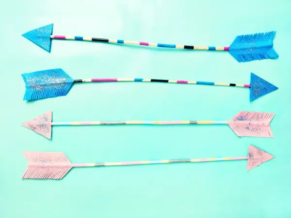 Vier bunte Pfeile zum Basteln, mit Glitzer verziert und auf hellblauem Hintergrund arrangiert.