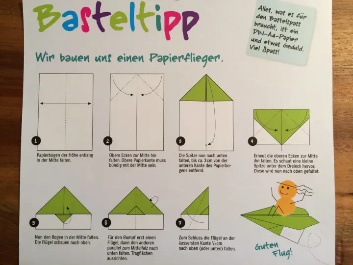 Anleitung zum Papierflieger basteln mit 7 Schritten. Ein kleiner gelber Smiley sitzt auf dem fertigen grünen Papierflieger.