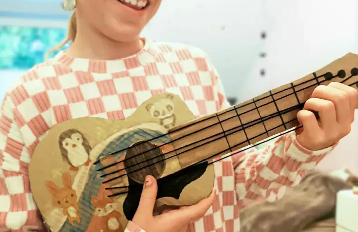Kind bastelt Gitarre nach Vorlage. Die selbstgemachte Gitarre ist mit süßen Tieren wie Pinguin, Panda, Hase und Fuchs bemalt.