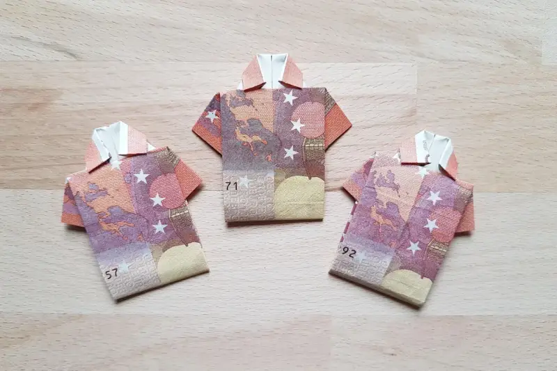 Drei Origami-Hemden aus Geldscheinen. Das letzte Hemd falten ist eine Kunst für sich.
