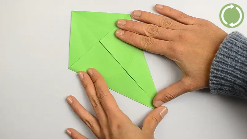 Hände falten ein grünes Papier, um einen einfachen Drachen zu basteln.